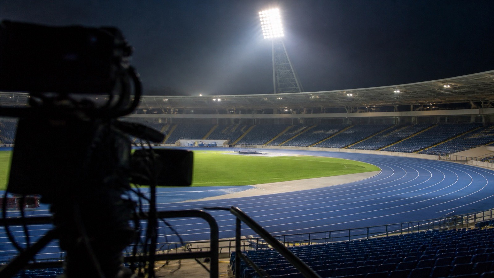 Friidrottsarena i kvällsljus med TV-kamera i förgrunden inför direktsändning